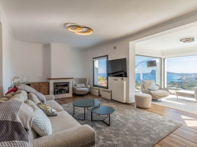 Modernes Wohnzimmer mit hellem Sofa, Kamin und großen Fenstern, die einen Panoramablick auf Meer und Stadt bieten. Die zeitgenössische Einrichtung hellt den Raum auf.