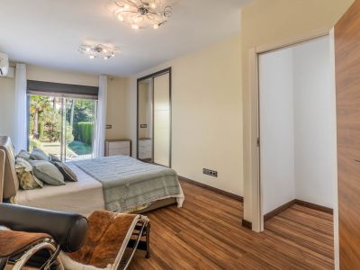 Schlafzimmer mit direktem Gartenzugang durch Glasschiebetüren, Laminatboden und Spiegelschiebetürenschrank. Ein offener Ankleidebereich ist sichtbar.