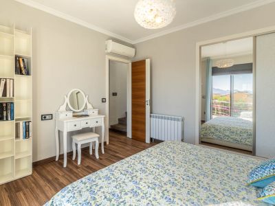 Schlafzimmer mit Laminatboden, weißem Schminktisch und modularem Bücherregal. Der Spiegelschrank reflektiert einen Bergblick vom Balkon.