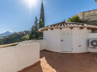Terrasse mit Terrakottafliesen und einem charmanten Nebengebäude mit traditionellem Ziegeldach. Bietet weitreichende Ausblicke auf grüne Hügel und ferne Berge unter klarem Himmel.