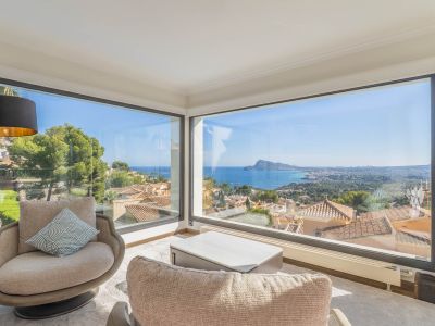 Wohnbereich mit großen Eckfenstern, die einen Panoramablick auf das Meer und die Küste freigeben. Zwei Sessel und ein moderner Couchtisch gestalten diesen hellen Raum.