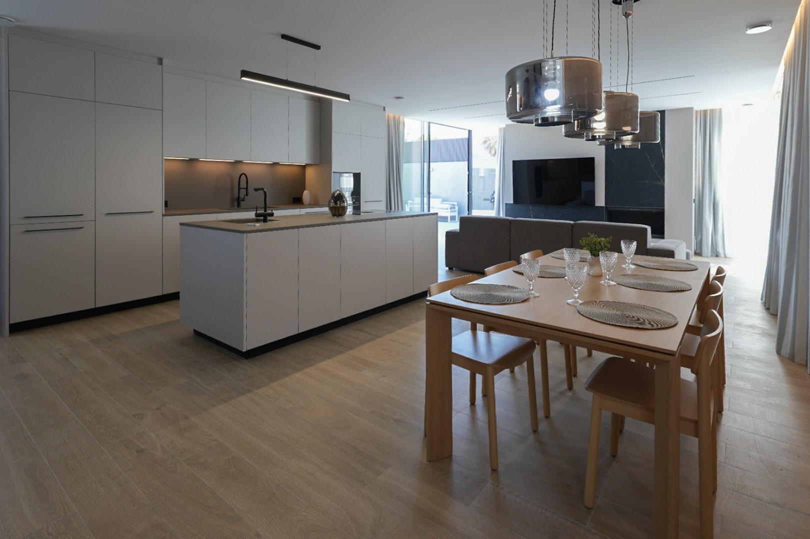 Minimalistische Designküche mit zentraler Insel und schwarzer Armatur, offen zum eleganten Essbereich aus Holz mit sechs Stühlen und modernen Pendelleuchten.