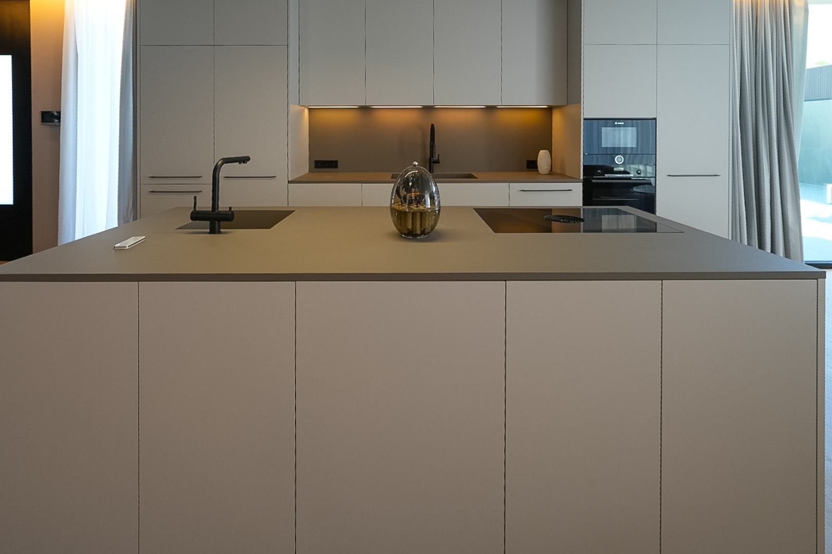 Moderne Designküche mit zentraler Insel, integriertem Spülbecken, Induktionskochfeld und neutralen Schränken.