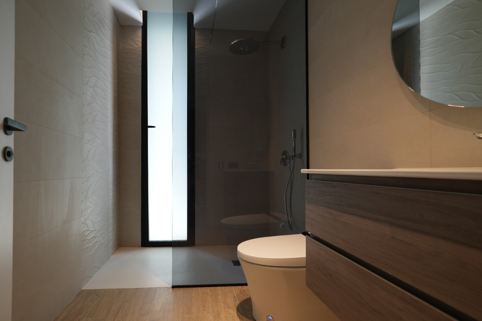 Modernes Badezimmer mit Holzwaschtisch, Rundspiegel und begehbarer Dusche. Strukturierte Wandfliesen und ein Milchglasfenster.