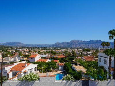 Erhöhte Ansicht des Wohngebiets von Albir, mit privatem Pool, Häusern mit Ziegeldächern und üppiger mediterraner Vegetation, vor einer Bergkulisse.