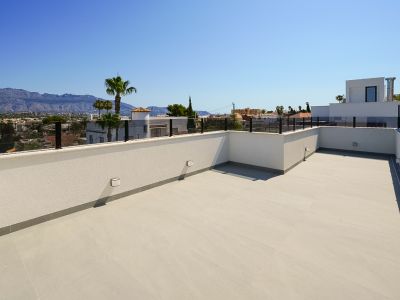 Geräumige Dachterrasse mit hellen Bodenfliesen und moderner Glasbrüstung, mit Panoramablick auf die Berge und die umliegende Stadt.