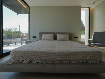 Hauptschlafzimmer mit schwebendem Bett, gepolstertem Kopfteil, großen Fenstern mit Meerblick und Sessel. Integrierte Nachttische.