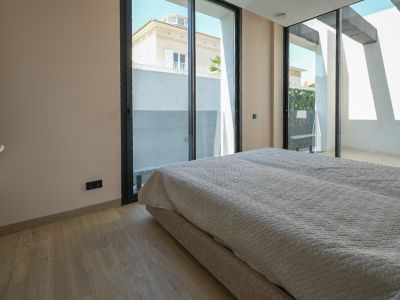 Helles Schlafzimmer mit hellem Holzfußboden und großen, schwarz gerahmten Glasschiebetüren, die den Blick auf ein Nachbarhaus und eine grüne Wand freigeben.