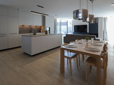 Minimalistische Designküche mit zentraler Insel und schwarzer Armatur, offen zum eleganten Essbereich aus Holz mit sechs Stühlen und modernen Pendelleuchten.