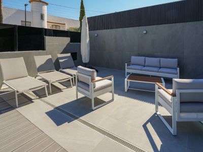 Moderne Außenterrasse mit Lounge-Möbeln in Weiß und Grau, kombiniertem Feinsteinzeug- und WPC-Boden. Sonnenliegen und eine Sitzgruppe sind vorhanden.