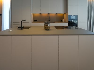 Moderne Designküche mit zentraler Insel, integriertem Spülbecken, Induktionskochfeld und neutralen Schränken.