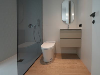 Modernes Badezimmer mit ebenerdiger Dusche, dunkler Glaswand und strukturierter grauer Wand, wandhängendem WC, schwebendem Waschtisch und hellem Holzfliesenboden.