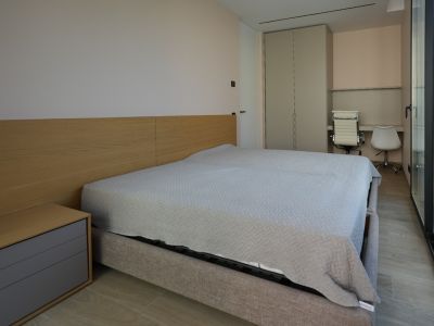 Modernes Schlafzimmer mit hellgrauem Polsterbett, Holzkopfteil und integriertem Nachttisch. Verfügt über Einbauschrank, doppelten Schreibtischbereich und große Glasfront.
