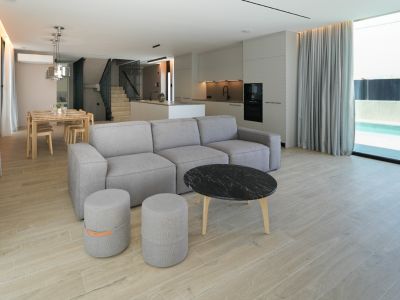 Offener Wohn- und Essbereich mit modularem Sofa, Marmor-Couchtisch und integrierter Küche, verbunden mit dem Außenpool durch große Fenster.
