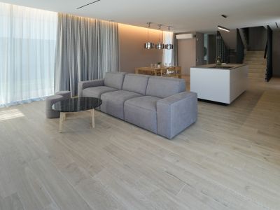 Offener Wohnbereich mit grauem Modulsofa, schwarzem Marmor-Couchtisch und holzoptik Fliesenboden. Große Fenster mit doppelten Vorhängen.