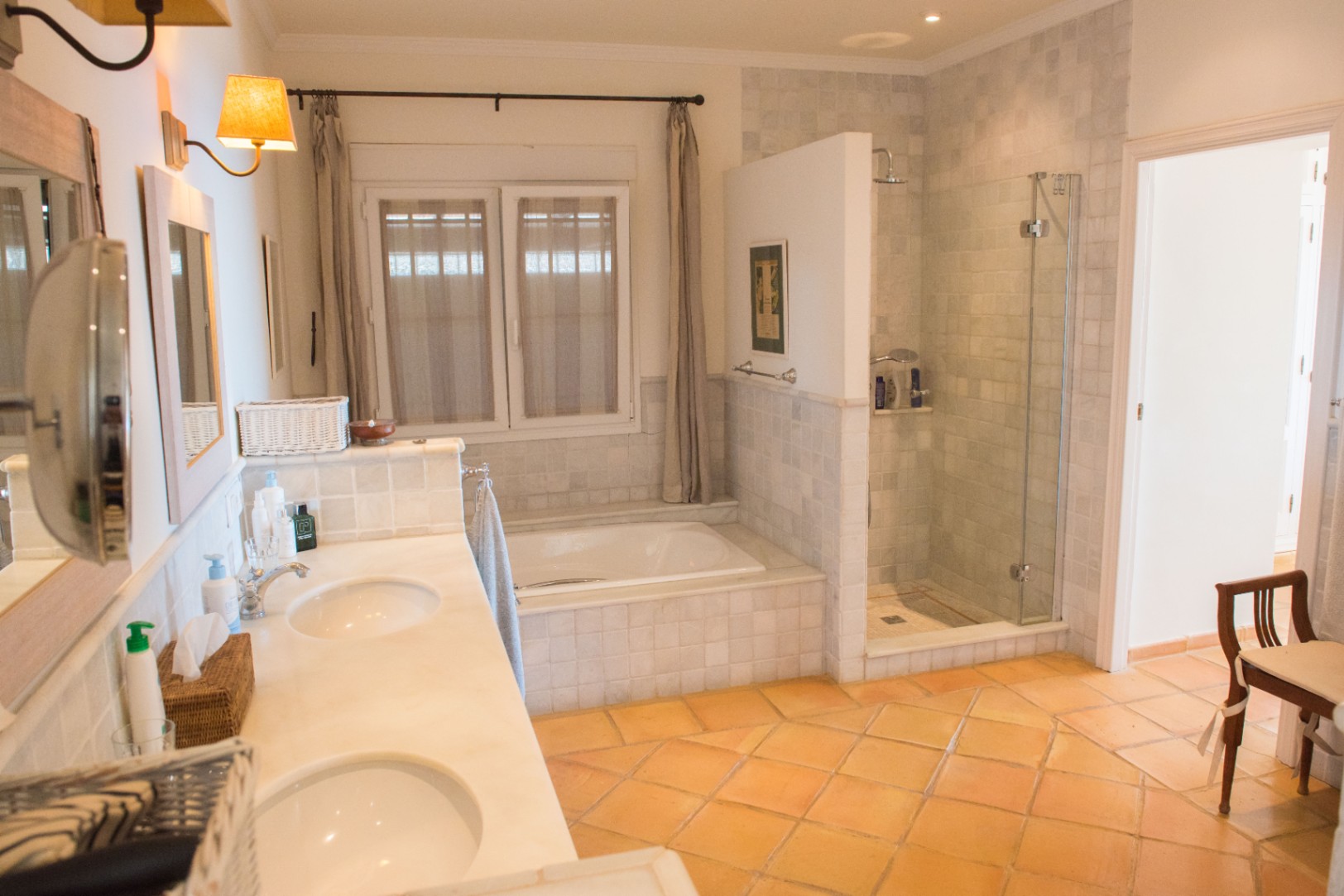 Großzügiges Badezimmer mit Doppelwaschtisch aus Marmor, Terrakottaboden, Einbaubadewanne und separater begehbarer Dusche mit Glastür.