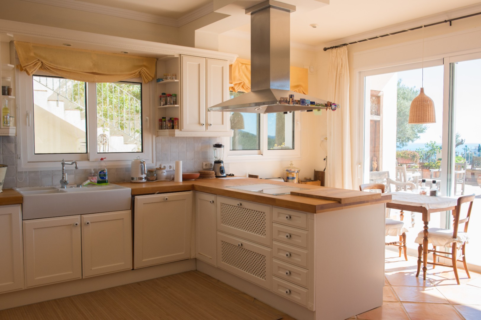 Küche im Landhausstil mit weißen Schränken, Massivholz-Arbeitsplatten, Keramikspülbecken und Edelstahl-Abzugshaube mit direktem Zugang zur Terrasse.