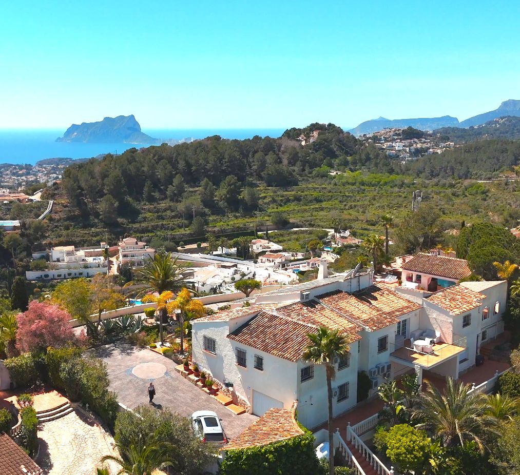 Luftaufnahme der mediterranen Villa mit Terrakottadächern, gepflegten Gärten und Panoramablick auf das Meer und den markanten Peñón de Ifach.