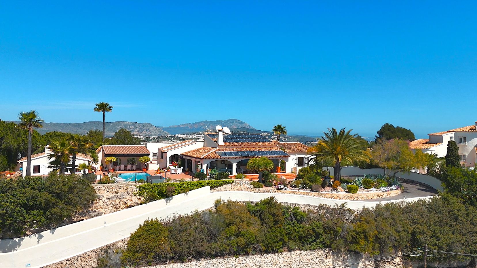 Luftaufnahme der Villa mit Terrakottadächern, Sonnenkollektoren und Pool, eingebettet in mediterrane Gärten mit Panoramameerblick.