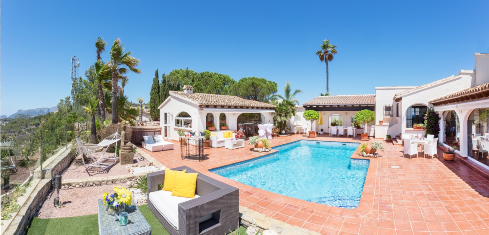 Terrasse mit rechteckigem Pool, Terrakottaboden und verschiedenen Sitzbereichen. Die mediterrane Architektur besticht durch weiße Wände und Rundbogenfenster.
