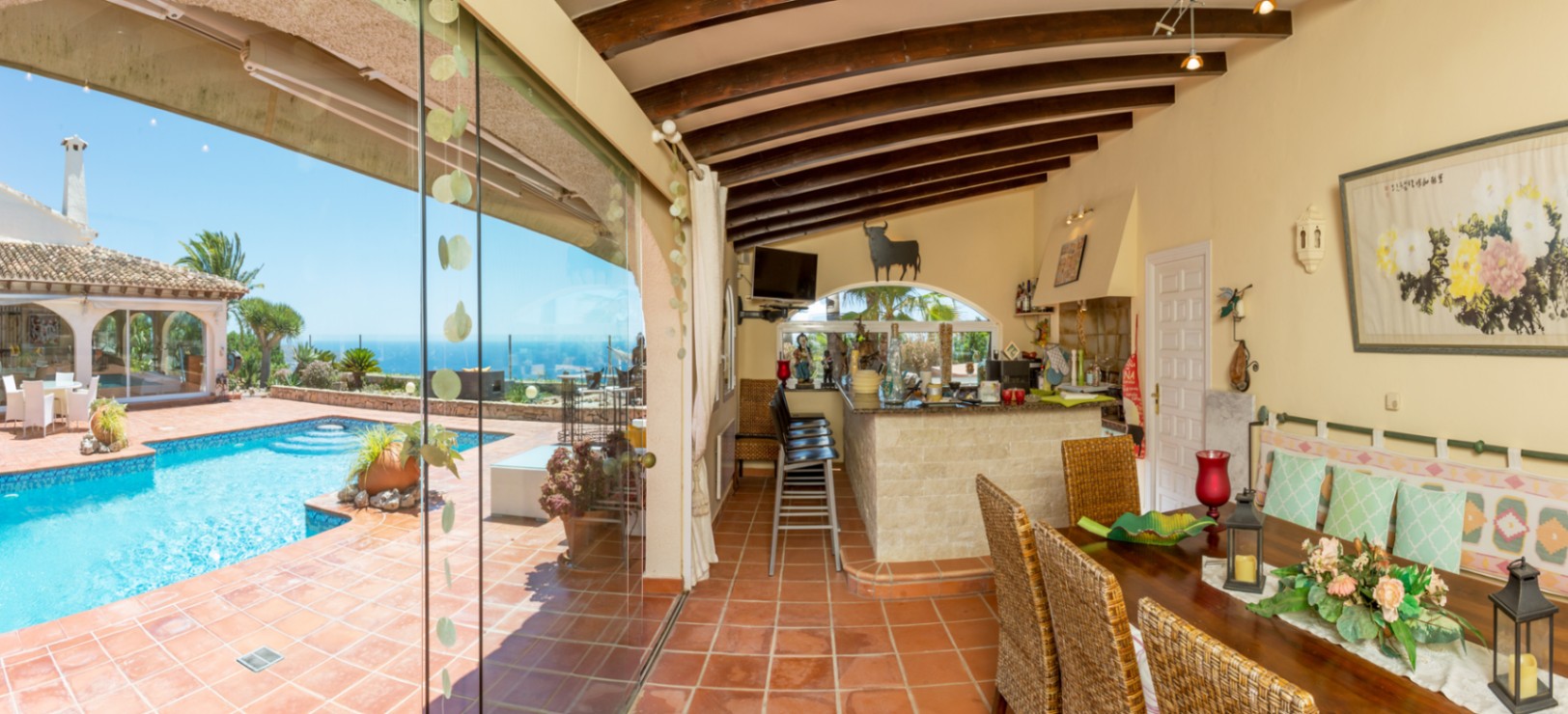 Überdachte Terrasse mit Holzbalkendecke, Terrakottafliesen und einer Außenbar aus Stein, mit direktem Zugang zum Pool und weitem Meerblick.
