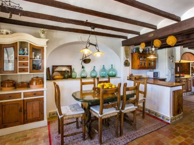 Rustikaler Essbereich mit ovalem Tisch, Holzstühlen und traditionellem Schrank. Sichtbare Holzbalken an der Decke.