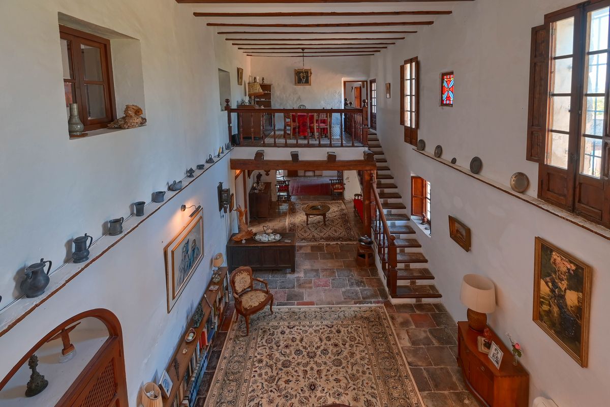 Großzügige, doppelt hohe Halle mit originalen Terrakottaböden, Sichtbalkendecke und einer Holztreppe, die zu einer Galerie mit rustikalem Geländer führt.