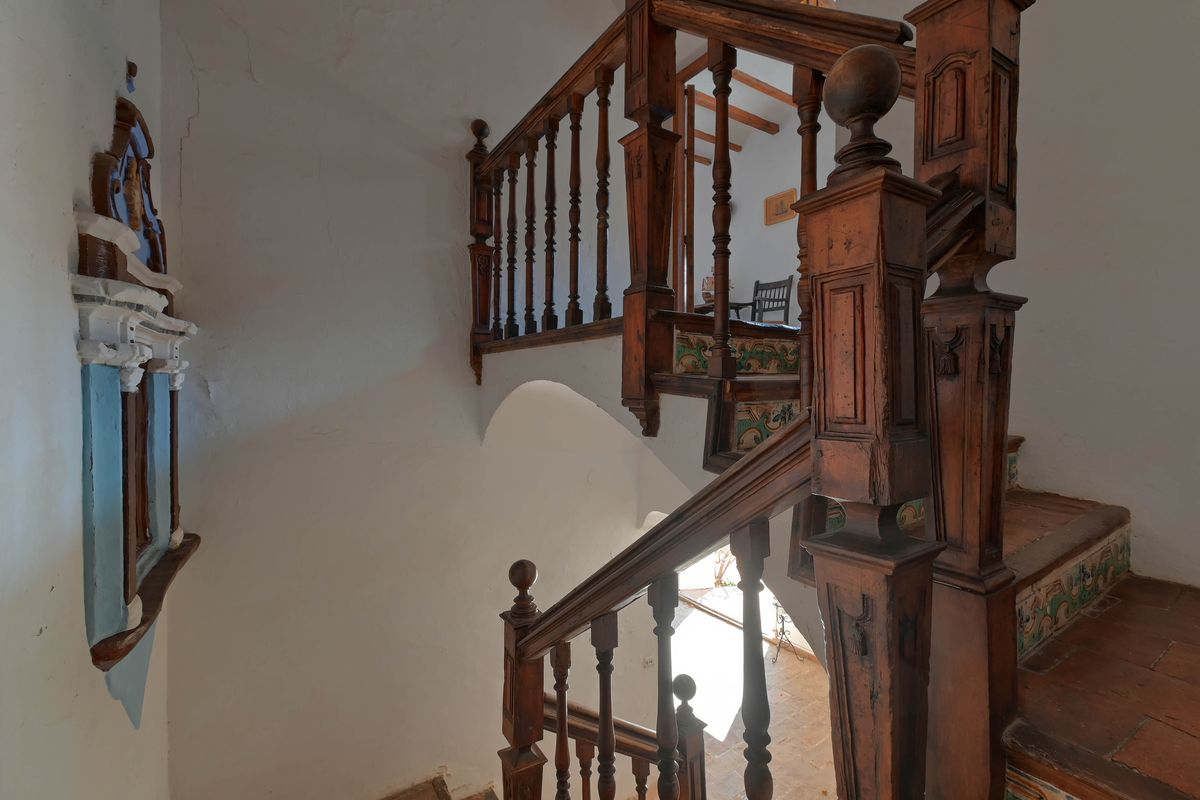 Historische Holztreppe mit geschnitzten Balustraden, Terrakotta-Stufen und traditionell dekorierten Keramikfliesen an den Setzstufen.