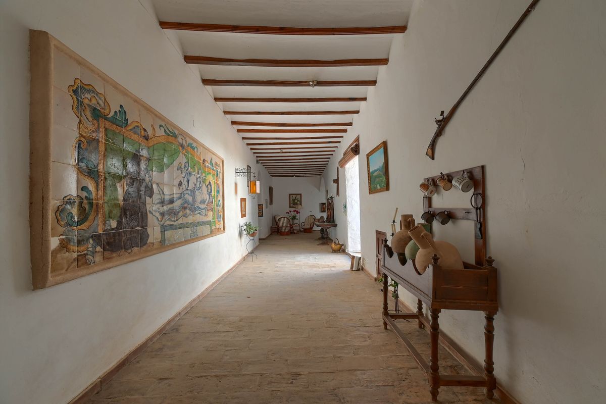 Historischer Flur mit Sichtbalkendecke, Natursteinboden und einem großen, handbemalten Keramikfliesen-Wandbild an der Wand.