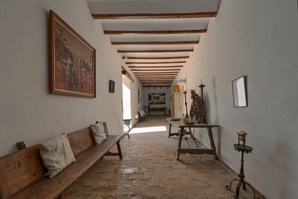 Historischer Flur mit sichtbaren Deckenbalken aus Holz, rustikalem Steinboden und antiken Möbelstücken in hellem Ambiente.