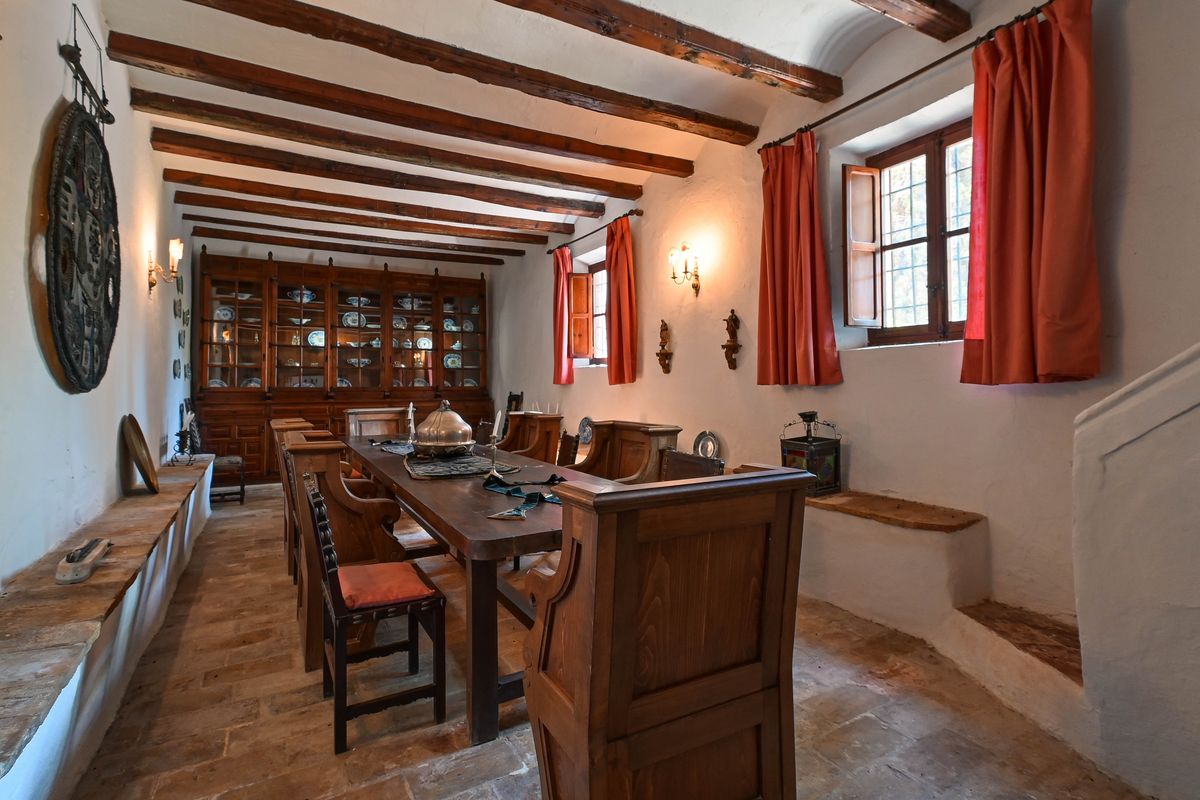 Historisches Esszimmer mit sichtbaren Holzbalken, Terrakottaboden und einem großen Einbauschrank aus Holz mit traditionellem Geschirr.