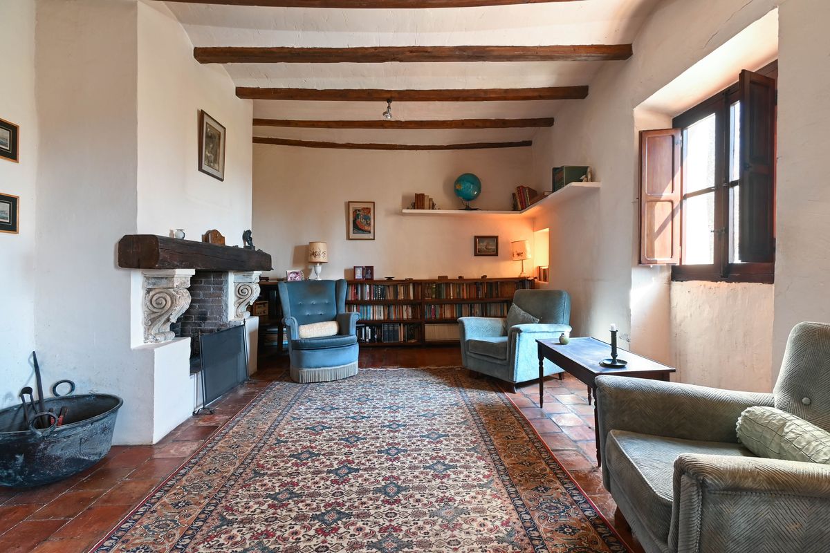 Historisches Wohnzimmer mit Sichtbalkendecke, großem Kamin mit Holzbalken, Terrakottaboden und integrierten Bücherregalen.
