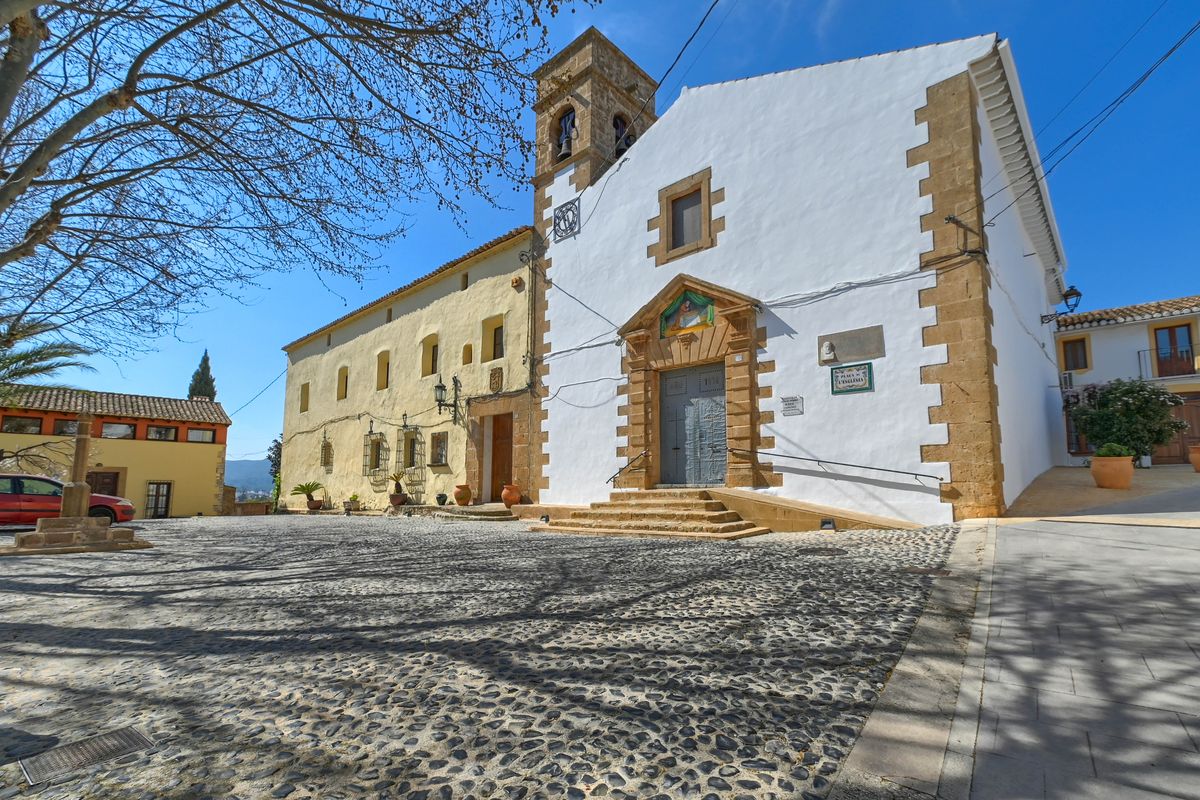 Kirchplatz in Jesús Pobre mit traditionellem Kopfsteinpflaster, weißer Fassade mit Natursteinelementen und historischem Glockenturm.