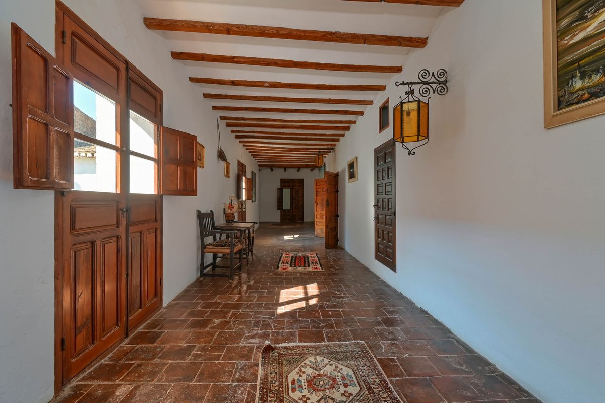 Langer Flur mit sichtbaren Deckenbalken aus Holz, authentischen Terrakotta-Fliesen und massiven Holztüren mit traditionellen Fensterläden.