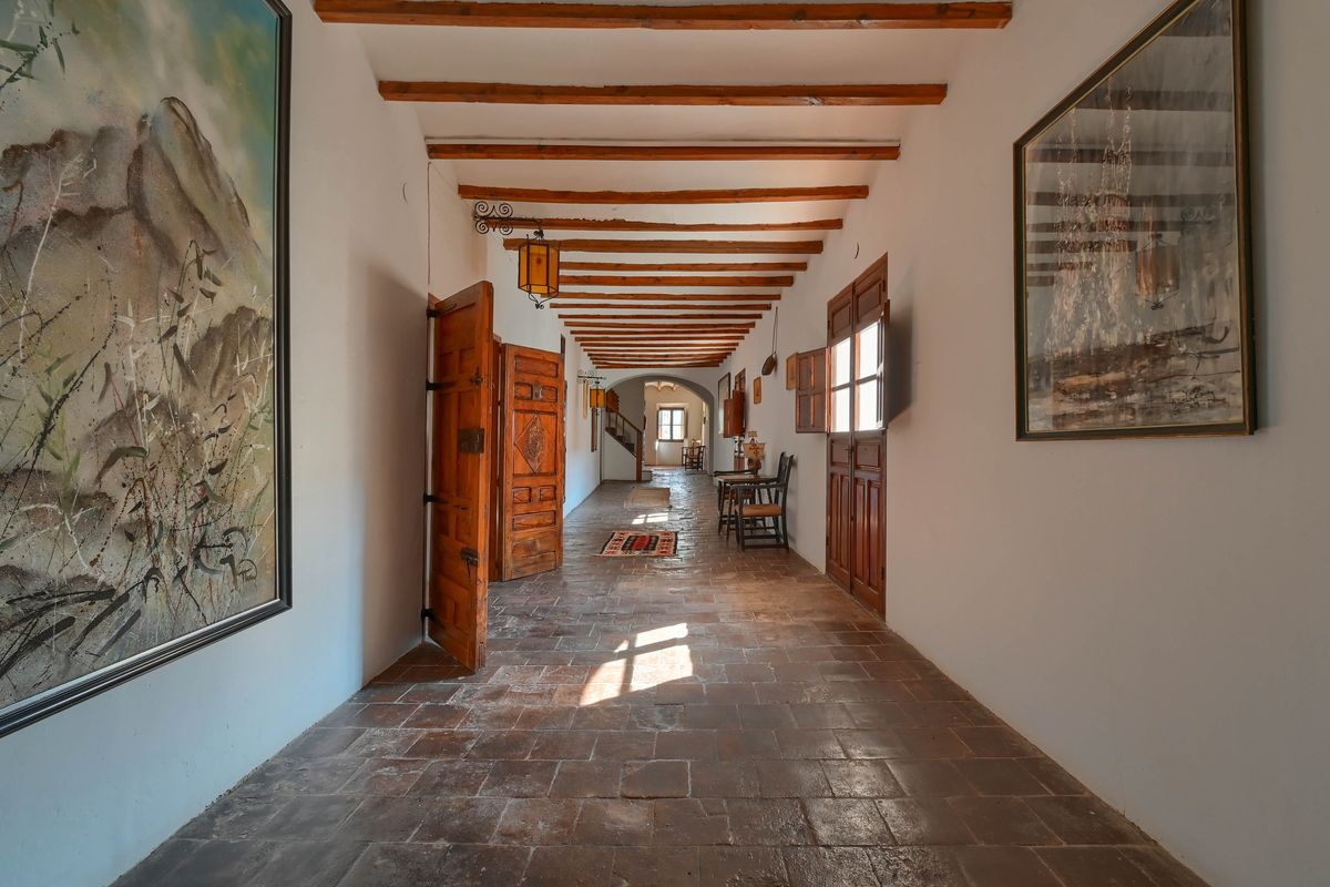 Langer Korridor mit traditionellen Terrakottafliesen, sichtbaren Deckenbalken aus Holz und massiven, handgearbeiteten Holztüren.