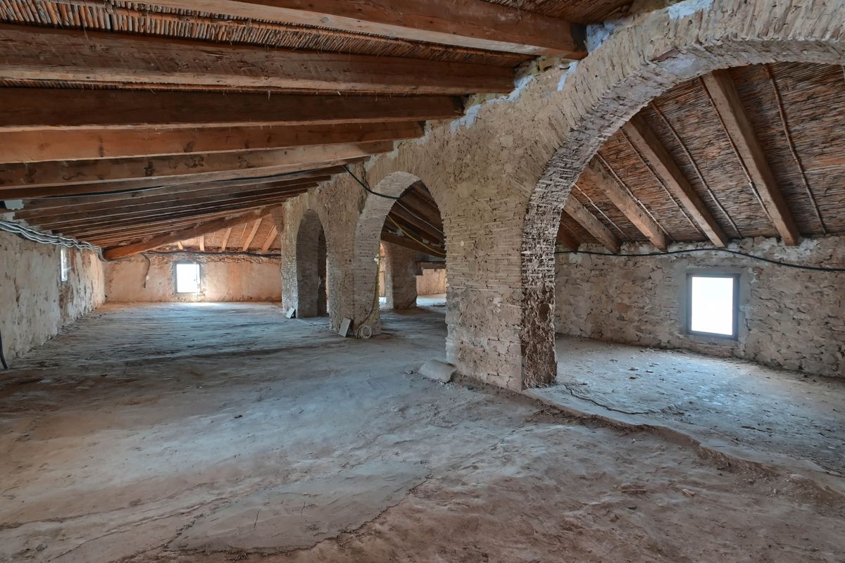 Offener Dachboden mit originalen Holzbalken, traditionellen Schilfrohrdecken und historischen Stein- und Backsteinbögen im Rohbauzustand.
