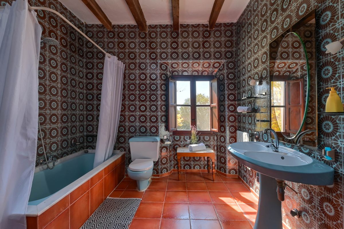 Rustikales Badezimmer mit geometrischen Wandfliesen, pastellblauen Sanitäranlagen, originalen Holzbalken und natürlichem Terrakottaboden.