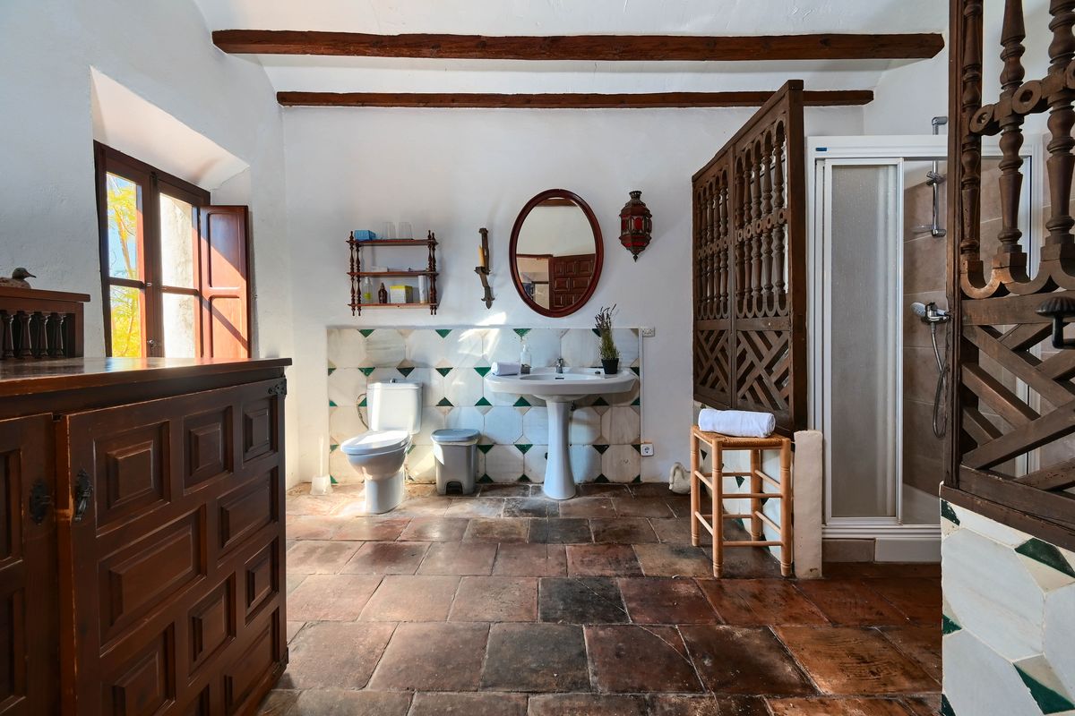 Rustikales Badezimmer mit Terrakottaboden, Holzbalkendecke und geschnitztem Holztrennelement. Ausgestattet mit einem Standwaschbecken und dekorativen Wandfliesen.