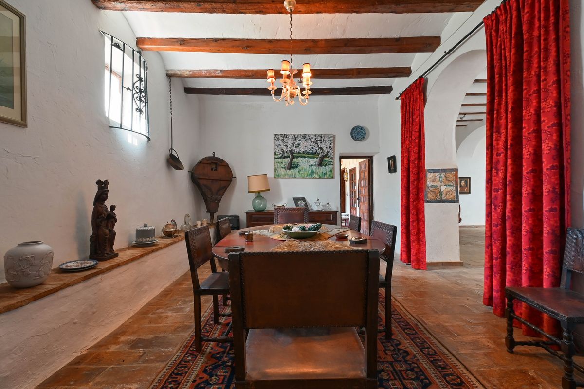 Rustikales Esszimmer mit sichtbaren Holzbalken, Terrakotta-Fliesenboden und traditionellen Ledersesseln neben einem Rundbogen mit Vorhängen.