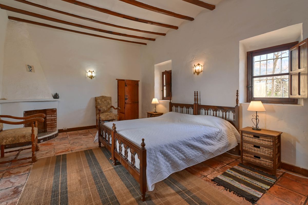 Rustikales Schlafzimmer mit Holzbalkendecke, Terrakottafliesen, einem gemauerten Kamin und Fenstern mit traditionellen Holzinnenläden.
