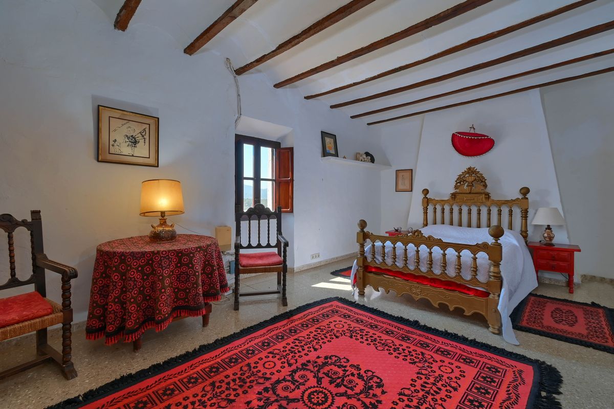 Rustikales Schlafzimmer mit originalen Holzbalkendecken, einem handgeschnitzten Bettgestell und roten Teppichen auf Steinboden.
