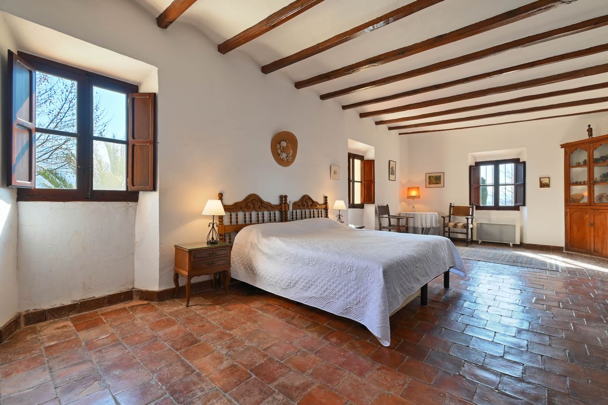 Rustikales Schlafzimmer mit sichtbaren dunklen Holzbalken, authentischen Terrakotta-Fliesen und traditionellen geschnitzten Holzmöbeln.