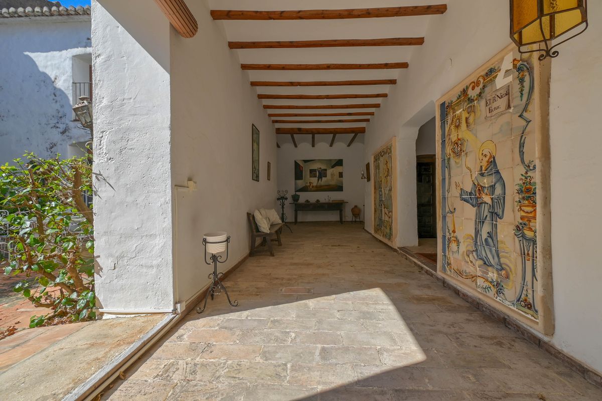 Traditionell überdachte Veranda mit sichtbaren Holzbalken, Natursteinboden und einem großen historischen religiösen Keramikmosaik an der Wand.