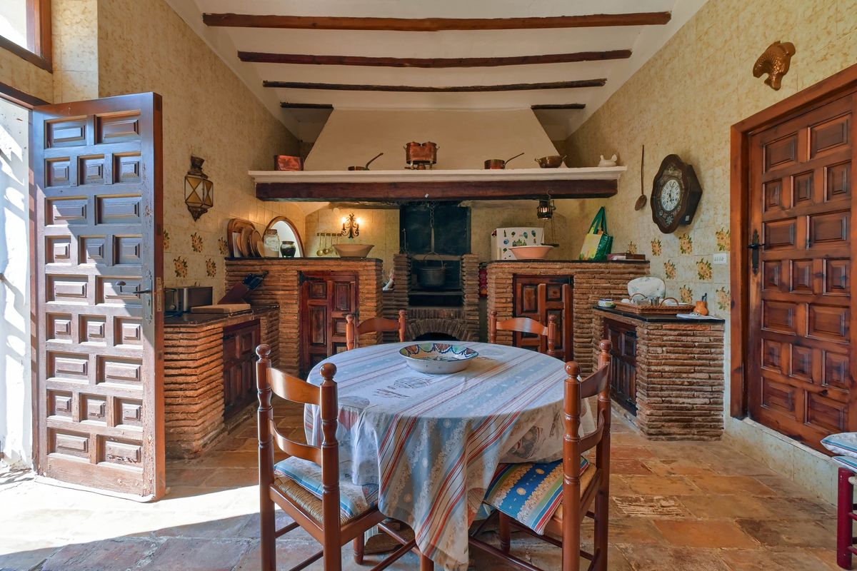Traditionelle rustikale Küche mit offenem gemauertem Kamin, sichtbaren Deckenbalken aus Holz und originalen Terrakottaböden.