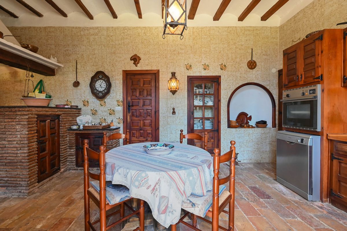 Traditionelle rustikale Küche mit Sichtbalkendecke, Terrakottaboden und gemauertem Herd. Wandfliesen mit Muster und integrierte moderne Elektrogeräte.
