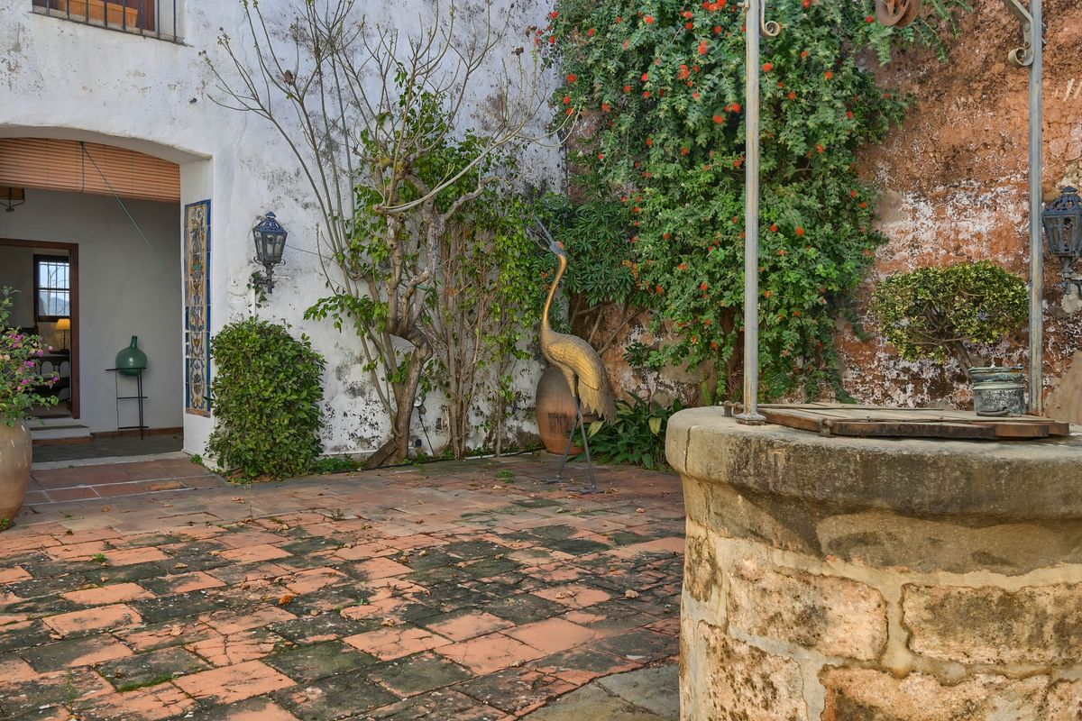 Traditioneller mediterraner Innenhof mit einem originalen Steinbrunnen, verwitterten Terrakottafliesen und einer dekorativen Kranichskulptur vor bewachsenen Mauern.