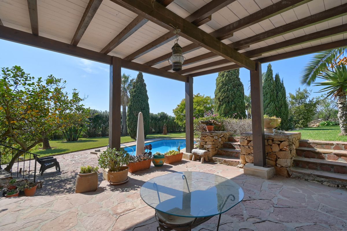 Überdachte Terrasse mit Holzbalken und Natursteinboden, mit Blick auf den privaten Pool und die gepflegte Gartenanlage.