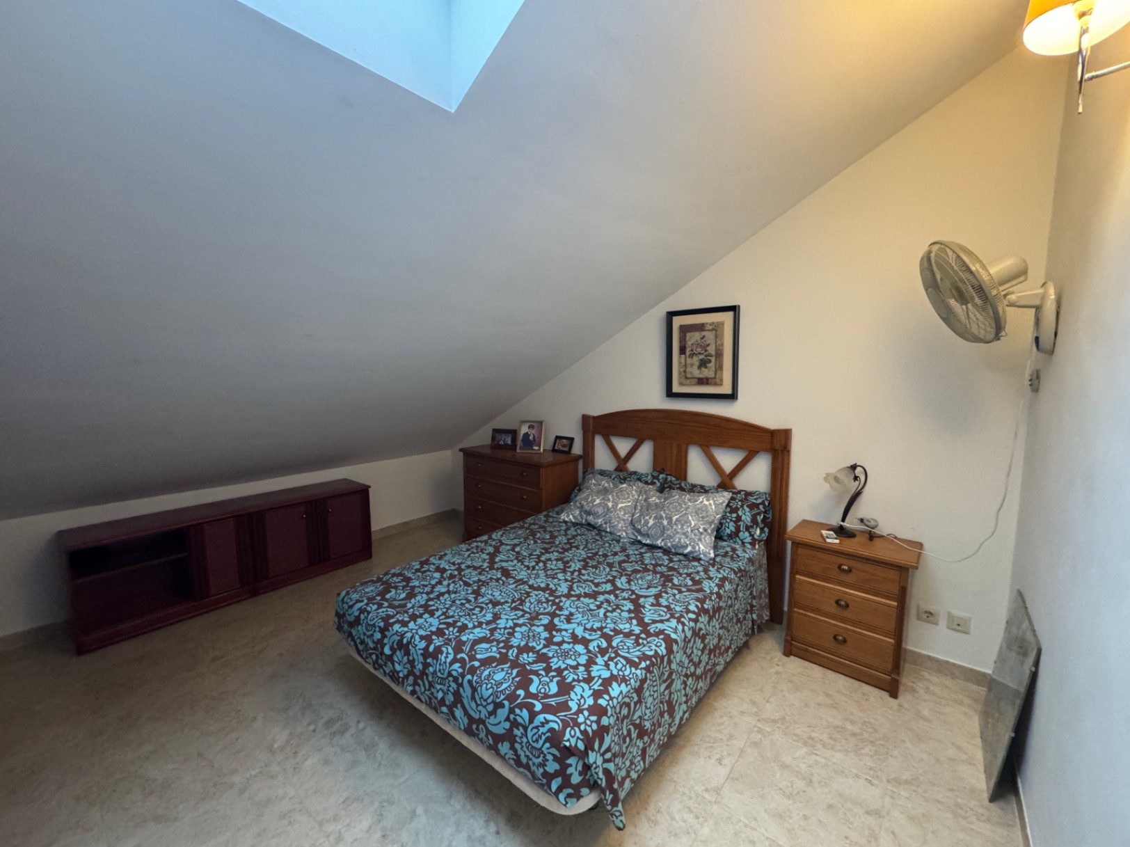 Dachgeschoss-Schlafzimmer mit Doppelbett, Holzkommode und Dachfenster.