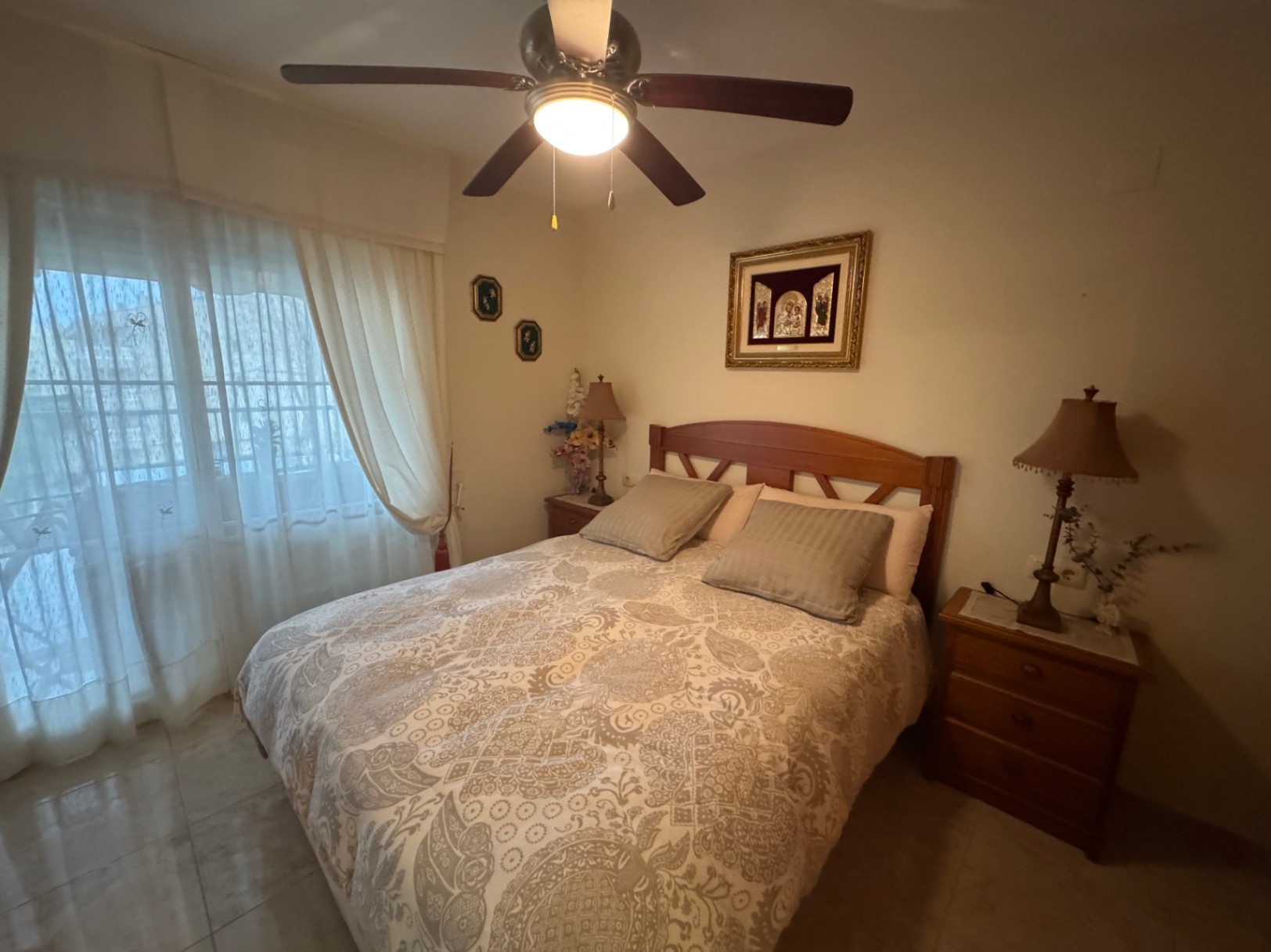 Schlafzimmer mit Holzbett, gemusterter Bettwäsche und Deckenventilator mit integriertem Licht.