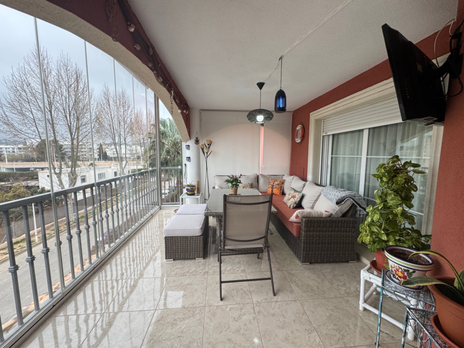 Überdachte Terrasse mit Glasverkleidung, Fliesenboden und Stadtblick.